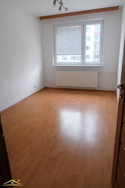 A room with a wooden decor floor in a 3-room apartment, with a bright interior and a window.