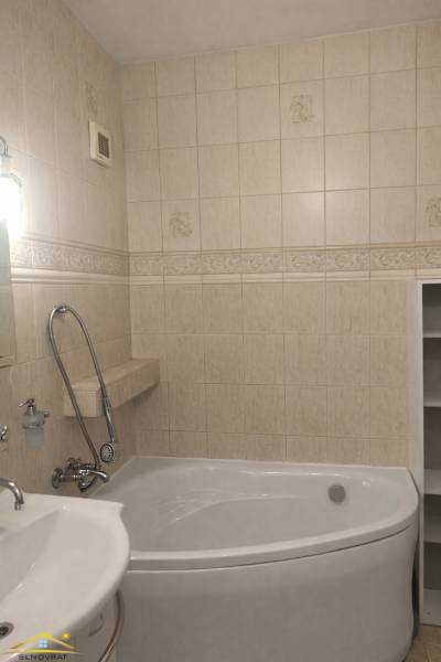 The bathroom of a three-room apartment with a bathtub and beige wall tiles.