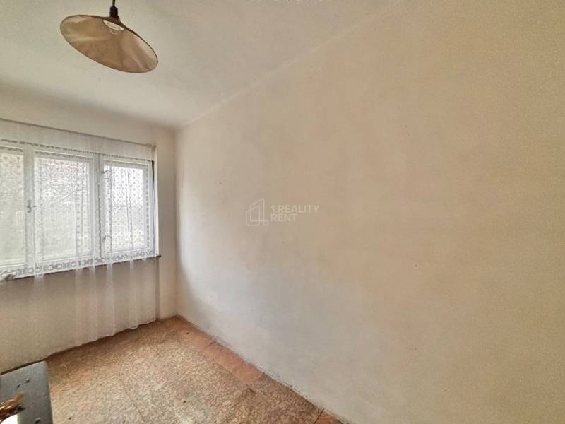A room in a family house with one window and a curtain, with carpeted flooring.