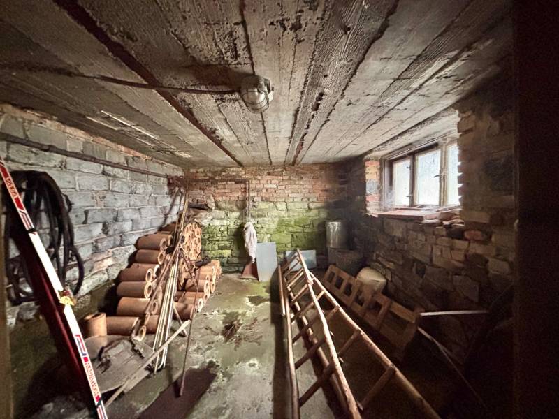Basement of a family house with brick walls and ceiling, stored pipes and tools.