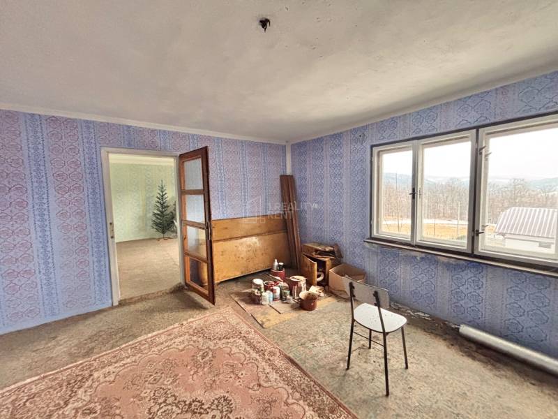 A room in a family house with blue wallpaper, old furniture, and a carpet.