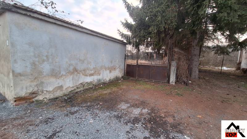 Land in Radzovce with an unplastered wall, metal gate, and conifer. Land - residential.