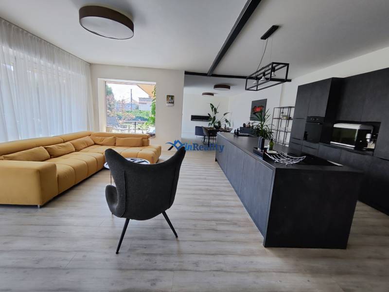 Living room with a large sofa and a modern kitchen, floor with wooden decor.