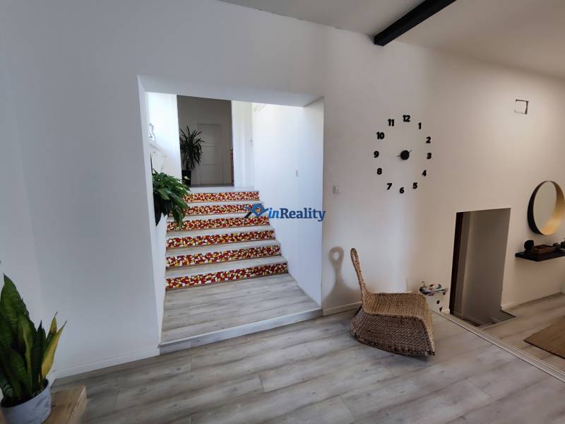 Interior of a family house with a clock on the wall, a floor with a wooden design, and stairs with a colorful pattern.