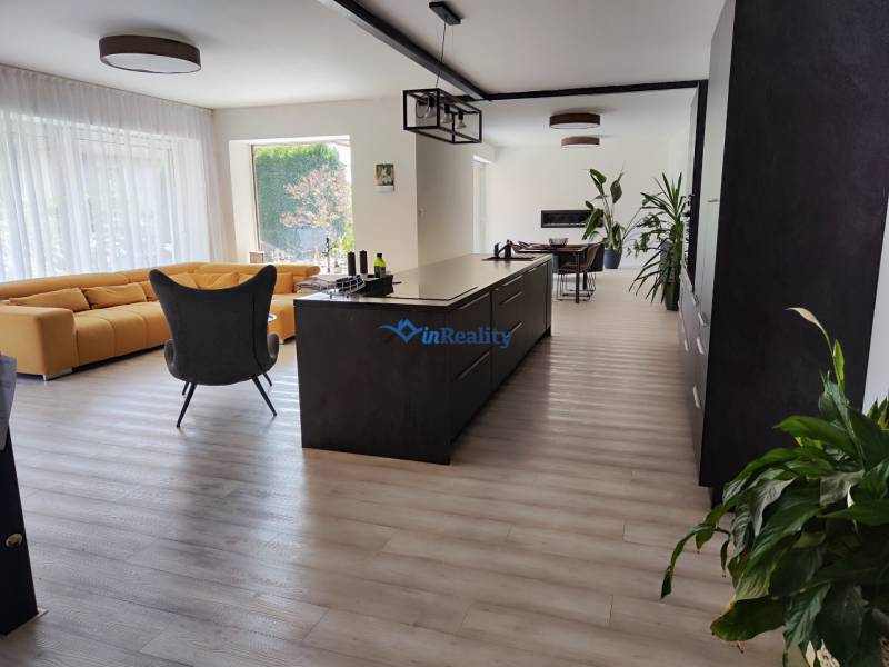 Kitchen and living room in a family house with an island, a yellow sofa, and a floor with a wooden decor.