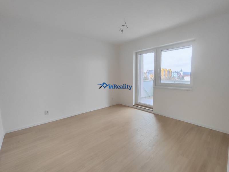 An empty room in a two-room apartment with a wood-patterned floor and balcony doors.