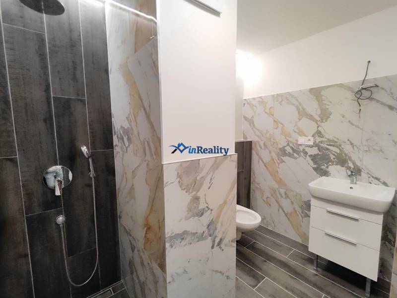 A bathroom in a 2-room apartment with marble tiles and a wooden decor floor.