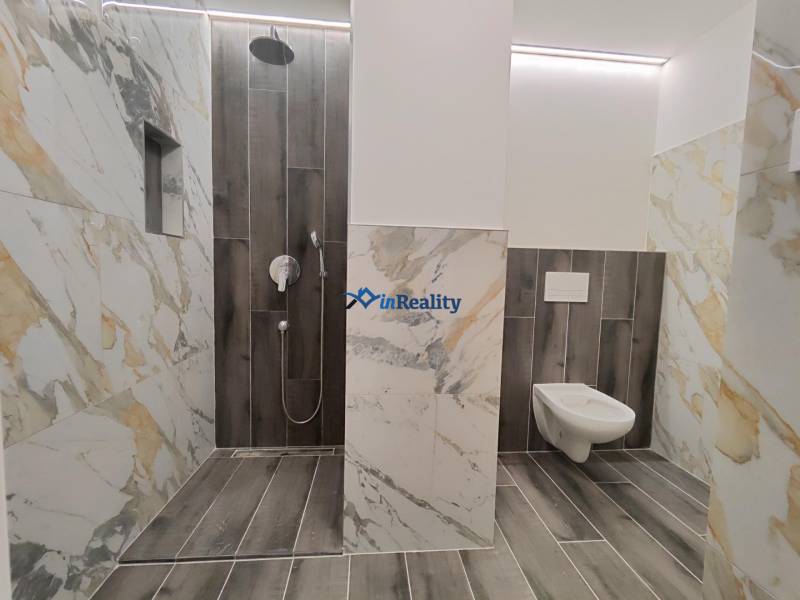 A bathroom in a 2-room apartment with marble tiles and a wooden decor floor.