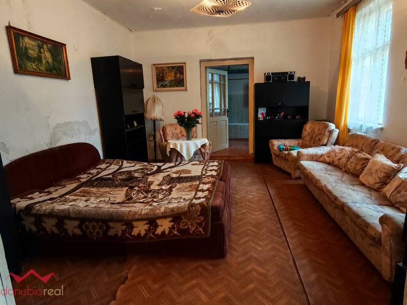 Living room in a family house with flowers, a sofa, and a wooden-patterned floor.