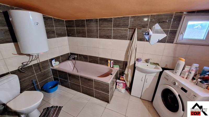 A bathroom in a family house with a bathtub, washing machine, and electric boiler.