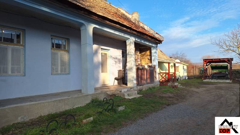 A family house in Rapovce with a blue facade and a large veranda. A yard with seating.