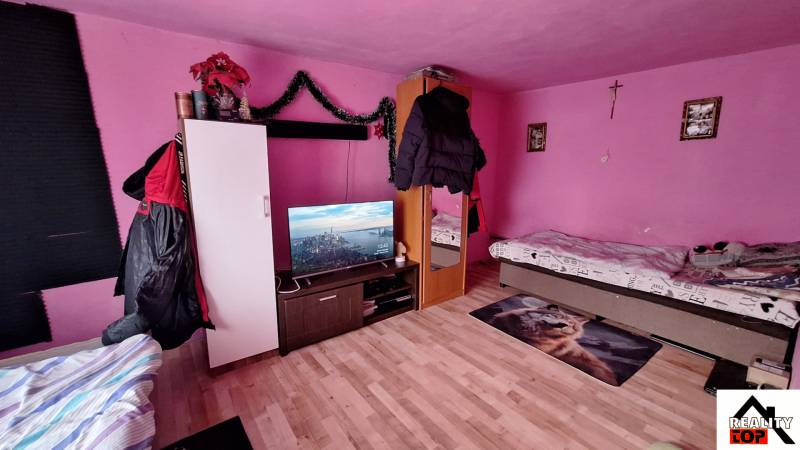 A pink room in a family house with beds, a television, and a wooden decor floor.