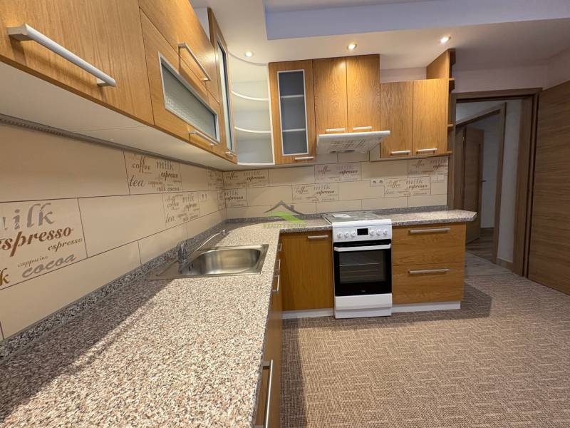 A kitchen with wooden cabinets and wallpaper in a 3-room apartment, flooring with a wooden decor.