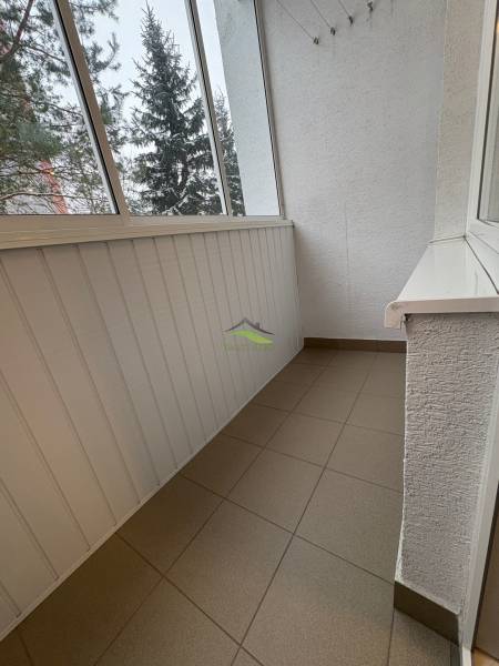 A glazed balcony in a 3-room apartment with ceramic tiles and a view of coniferous trees.