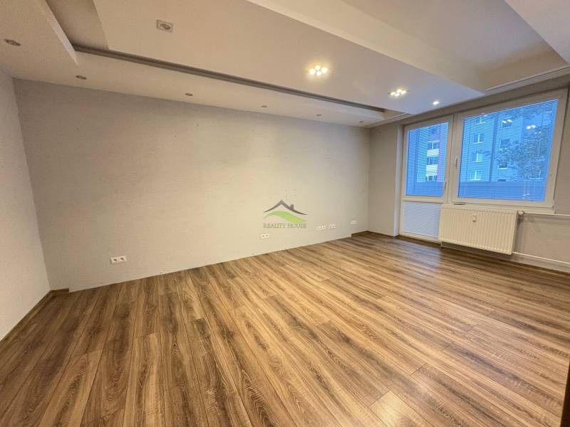 Living room in a three-room apartment with a wooden decor floor and a large window.