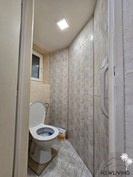 A bathroom in a one-room apartment with a toilet tiled in beige tiles.