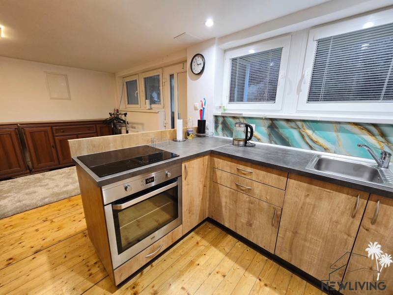 A kitchen in a studio apartment with a sink, electric oven, and wood-patterned flooring.