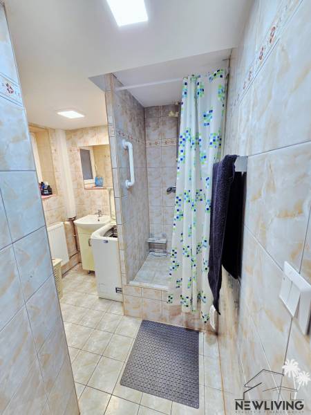 Bathroom in a studio apartment with tiles and a shower with a colorful curtain.