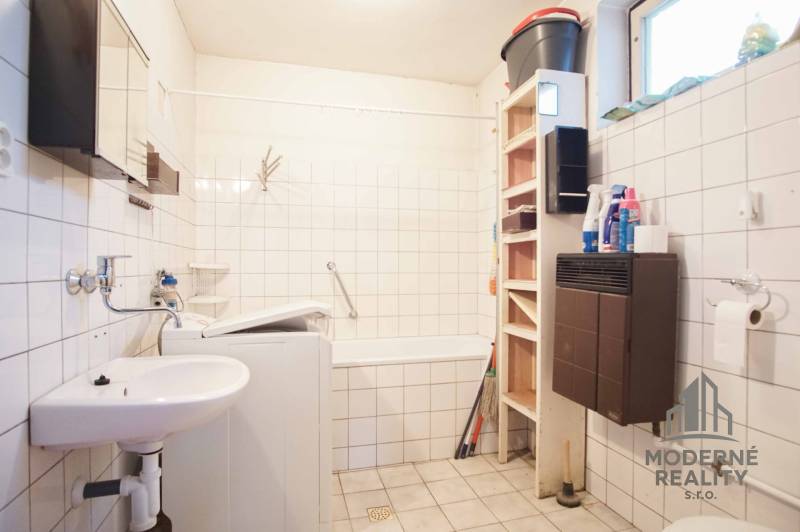 Bathroom in a family house with a bathtub, sink, washing machine, and shelving storage space.