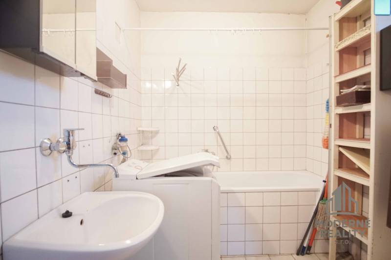 Bathroom in a family house with a bathtub, sink, and washing machine, white tiles.