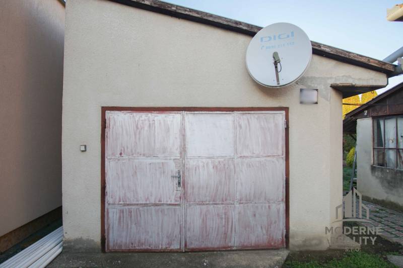 A garage with white doors next to a family house on Pod kopcom Street in Nové Zámky.