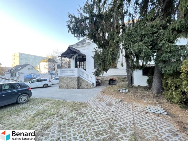 Building on Vajanského in Prešov with an access road, cars, and spruces in the foreground.