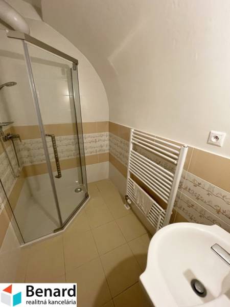 A bathroom in a building with ceramic tiles, a shower cabin, and a ladder radiator.