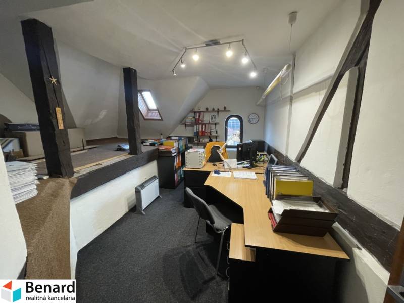 Office in a building with wooden beams, equipped with desks and office supplies.