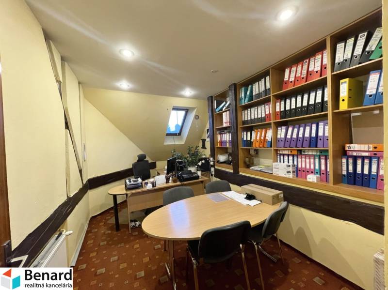 An office in a building with a slanted ceiling, desks, and shelves with documents.