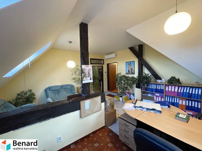 An office in a building with a wood-patterned floor, shelves for documents, and a seating area.
