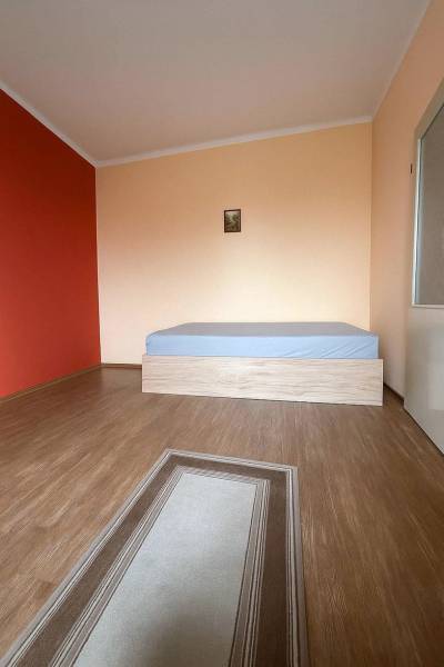 A room in a family house with a wooden decor floor, a bed, and a red wall.