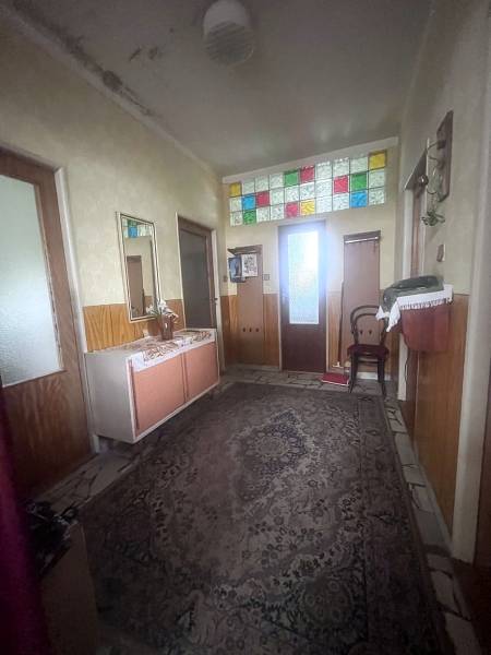 The hallway in the family house has a carpet and colorful stained glass windows above the doors.