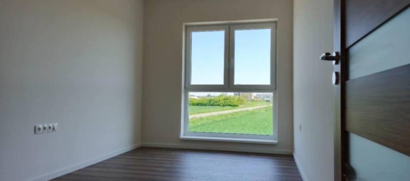 A bright room in a 3-room apartment with a wood-patterned floor and a large window.