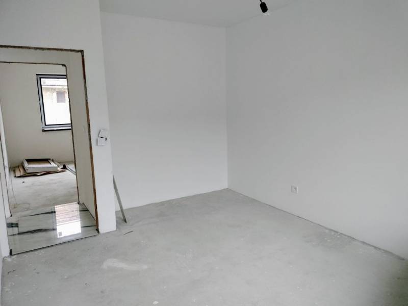 Empty room with white walls in a family house, with a door and a window visible.