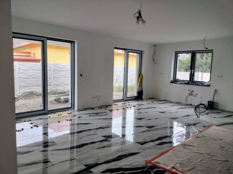 The living room of a family house with a glossy floor featuring a marble design and large windows.
