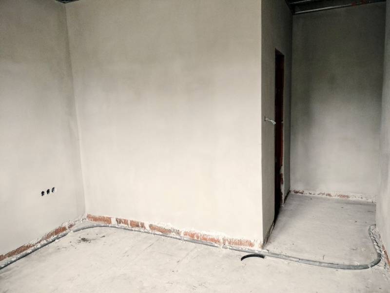 An unfinished interior in a family house with plastered walls and electrical installation preparation.
