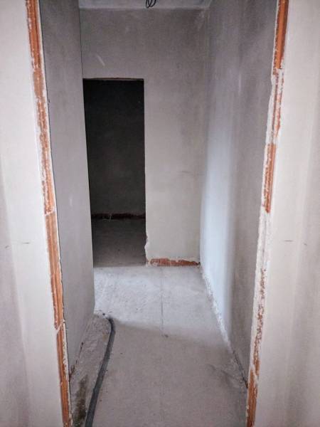 A narrow corridor in an unfinished family house with exposed wiring on the floor.