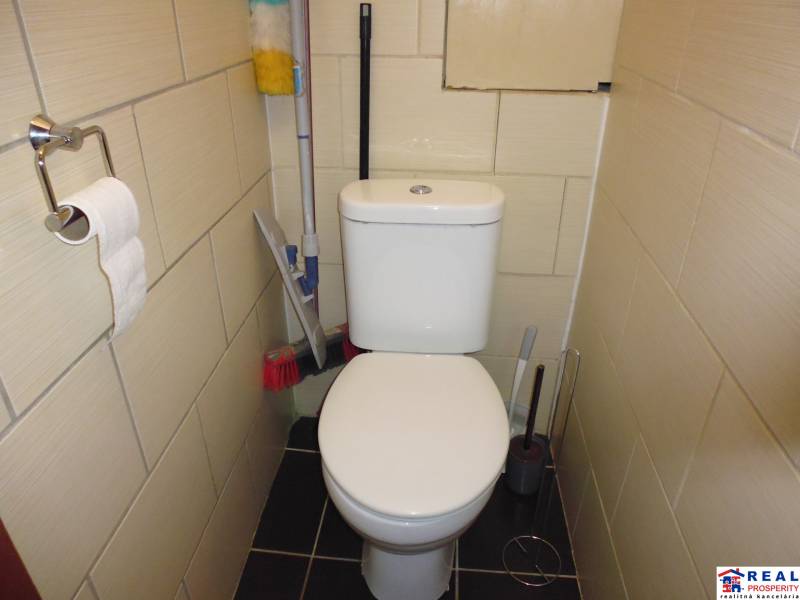 Bathroom in a 2-room apartment with a toilet, a scraper, and a toilet paper holder.