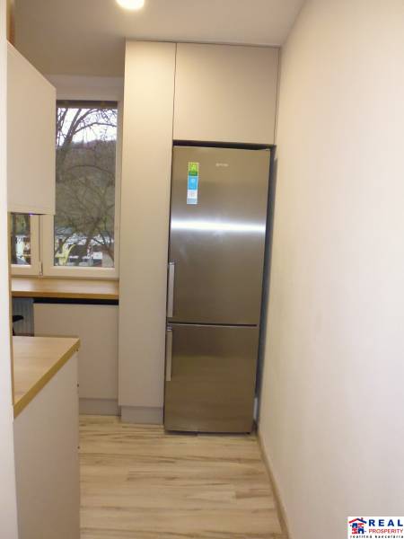 A kitchen with a wood-patterned floor and a refrigerator in a 2-room apartment.
