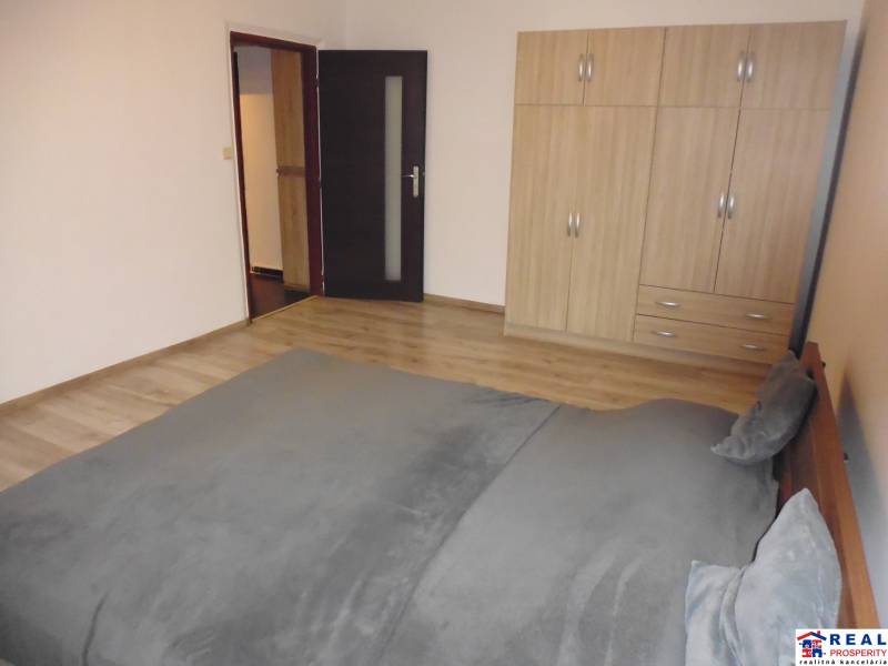 Bedroom in a two-room apartment with wood-patterned flooring, a bed, and a wardrobe.