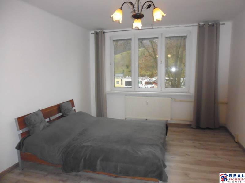 Bedroom in a 2-room apartment with a bed and wooden decor flooring, gray curtains.