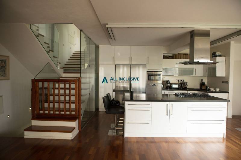 A kitchen in a family house with a wooden decor floor and glass staircase railing.