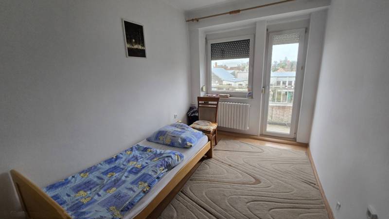 A bedroom with a single bed in a three-room apartment, with a view and a carpet.