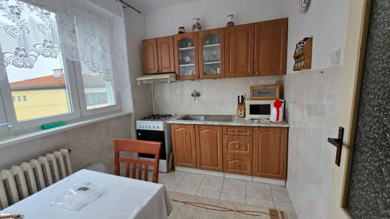 A kitchen in a 3-room apartment with a kitchen unit, stove, microwave, and table with a tablecloth.
