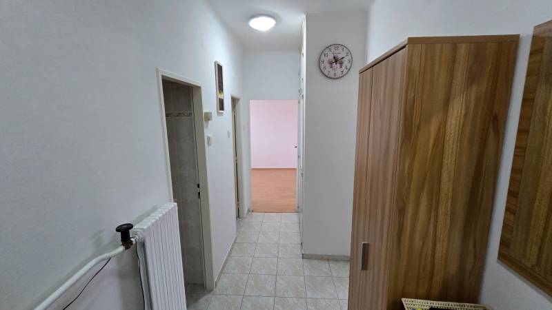 A hallway in a 3-room apartment with tiles, white walls, and wooden decor on the furniture.