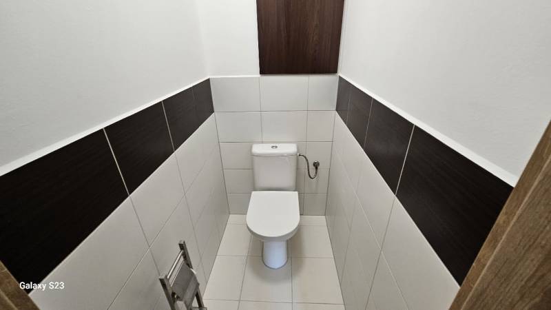A toilet with white tiles and dark stripes in a three-room apartment.