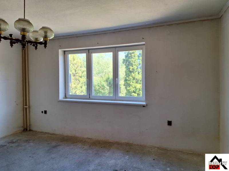 A room in a family house with a large window, an original chandelier, and a view of greenery.