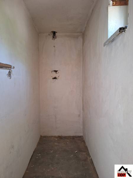 A narrow interior space in a family house with a small window and a concrete floor.