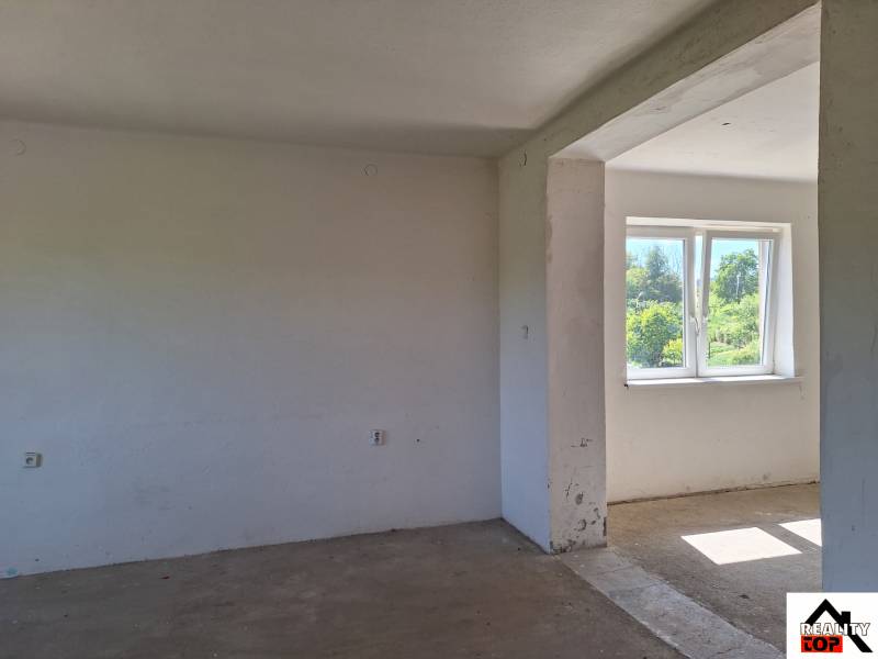 An unfurnished room in a family house with a view of the garden through a plastic window.
