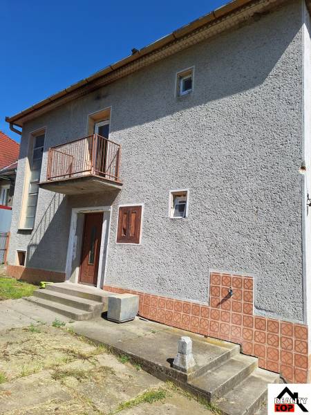 A family house in Šíd with a gray facade, a balcony, and concrete stairs in the exterior.